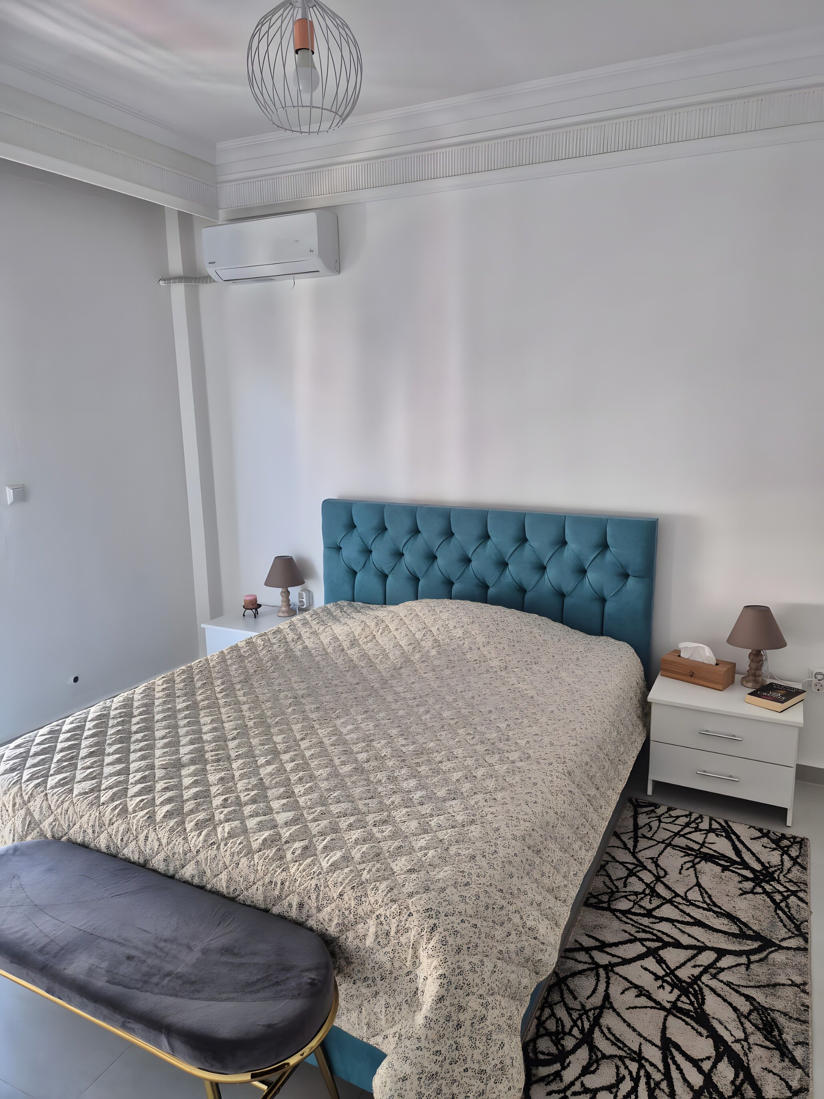 Ein Schlafzimmer mit einem Bett, Nachttischen, einer Bank und einem gemusterten Teppich.