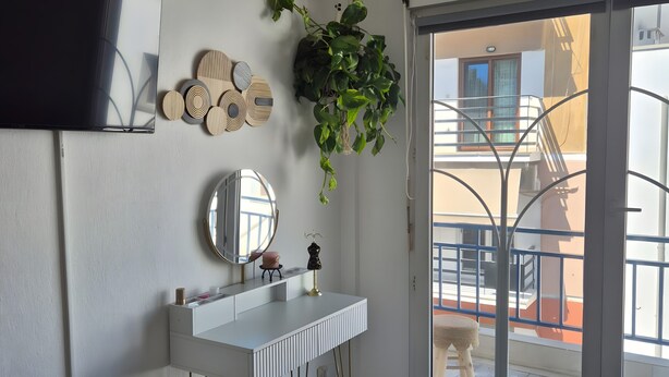 A bedroom with a white dresser, a mirror, a hanging plant, and a balcony with a dog. - Mokshouse – Bright, Comfortable Apartment near City Center and Beach (Kavala)