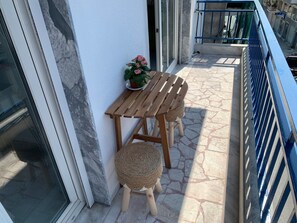 Un balcon avec une table et des chaises en bois, un pot de fleurs et une rambarde bleue.