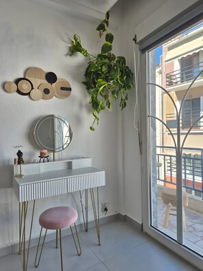 Ein modernes Badezimmer mit einem weißen Waschtisch, einem runden Spiegel, einer hängenden Pflanze und Blick auf den Balkon.