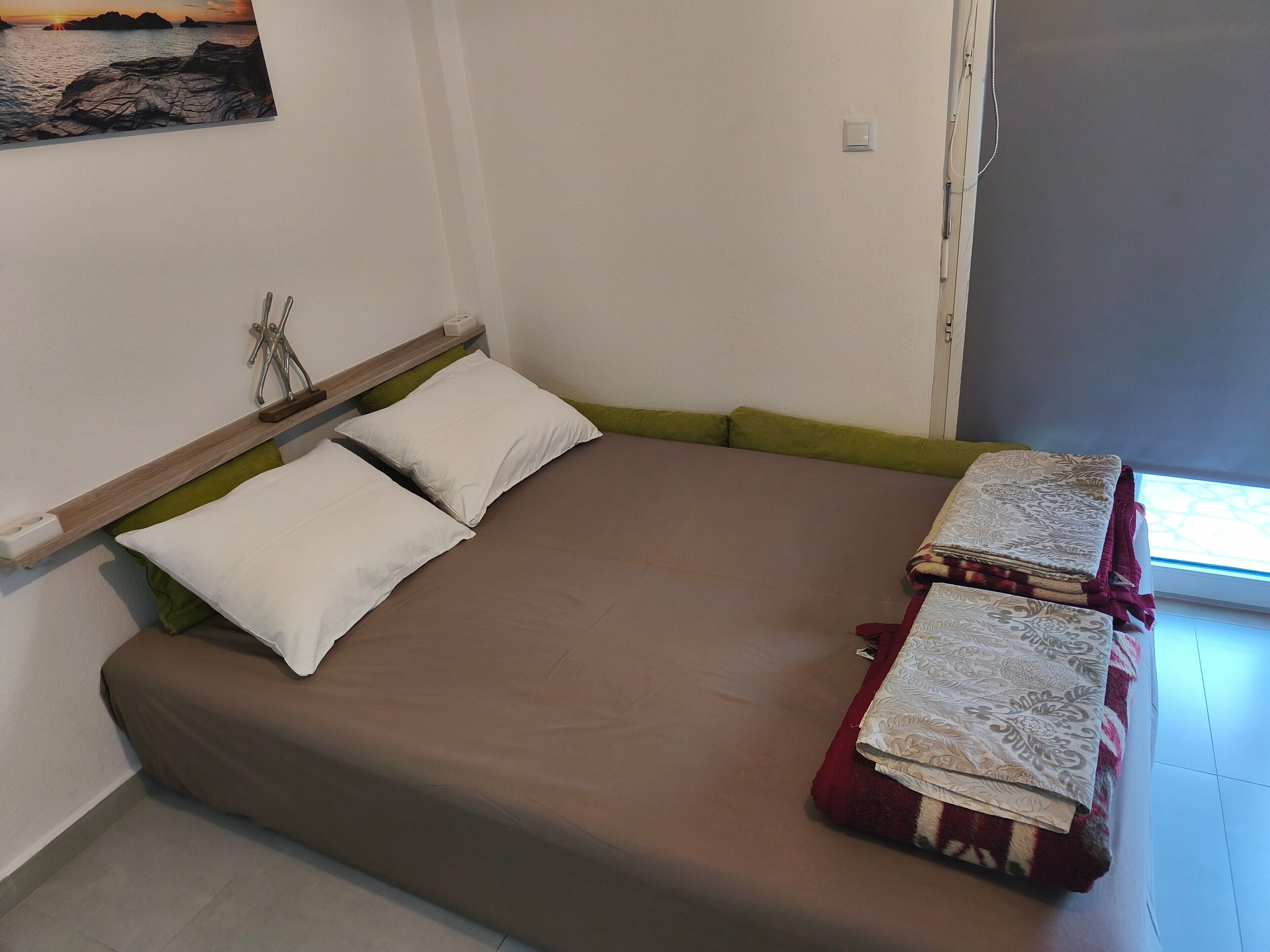 Een bed met een bruine matras, twee witte kussens en een groen hoofdbord.