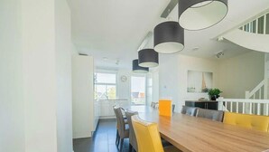 A modern dining area with a wooden table and yellow chairs, a kitchen in the background, and a staircase leading to an upper level. - Holiday Home in Uitdam With Terrace (Uitdam)