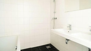 A bathroom with white tiled walls, a black tiled floor, a shower with a handheld showerhead, a sink with a mirror, and a toilet. - Holiday Home in Uitdam With Terrace (Uitdam)