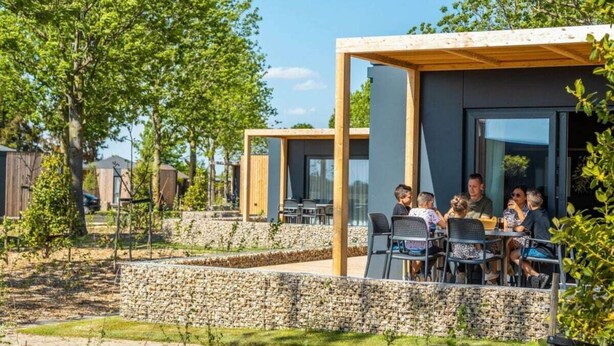 Een modern buitenzitgedeelte met een stenen muur en een houten pergola, omringd door groen.