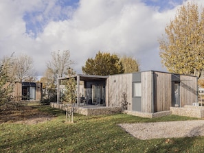 Ein modernes, eingeschossiges Haus mit Steinunterbau, Holzfassade und einer überdachten Terrasse.
