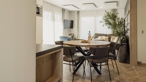 Een moderne eetruimte met een ronde tafel, meerdere stoelen, een televisie en een grote plant.