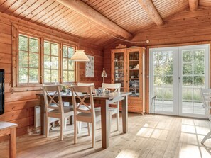 A wooden cabin interior with a dining table, chairs, a hanging lamp, a cabinet with glass doors, and a sliding glass door leading outside. - "Sigref" - 4km from the sea by Interhome (Ålbæk)