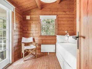 Ein Schlafzimmer einer Holzhütte mit einem Einzelbett, einem Heizkörper, einem Fenster und einem Klappstuhl.
