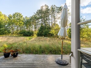 Eine Holzterrasse mit Sonnenschirm, Pflanzkübeln und Blick auf ein bewaldetes Gebiet.