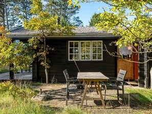 A wooden cabin with a window, a table, and two chairs in a natural setting. - "Sigref" - 4km from the sea by Interhome (Ålbæk)