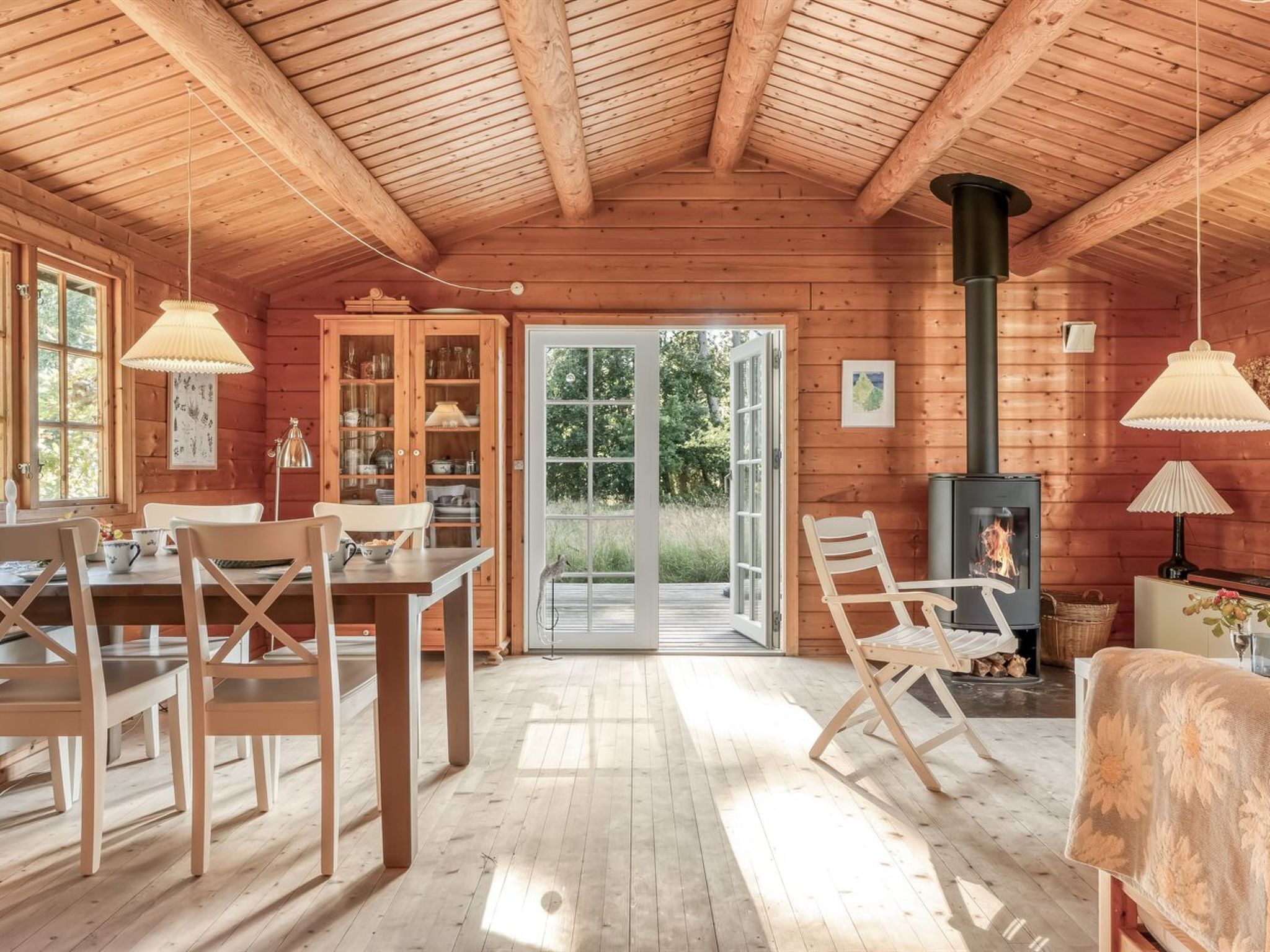A wooden cabin interior with a dining area, a fireplace, and a large glass door leading outside.