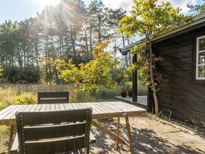 Eine Holzterrasse mit Tisch und Stühlen, umgeben von Bäumen und einer kleinen Holzhütte.