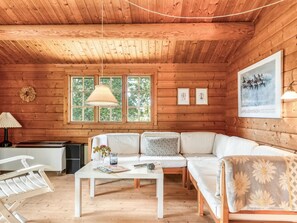 Ein gemütliches Blockhauss-Interieur mit Holzbalkendecke, einer Sofagarnitur, einem Tisch mit einer Vase und gerahmten Bildern an der Wand.