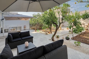 An outdoor seating area with a large umbrella, black sofas, and a small table with a vase.