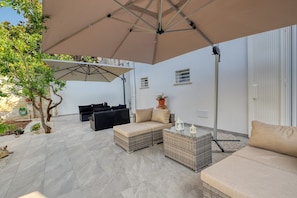 Een terras met tuinmeubilair, een grote parasol en een potplant.