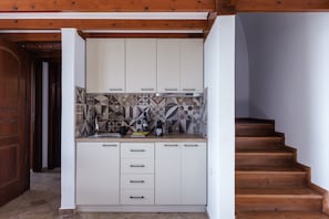 Eine Küche mit weißen Schränken, einer gemusterten Spritzschutzleiste und einer Holztreppe.