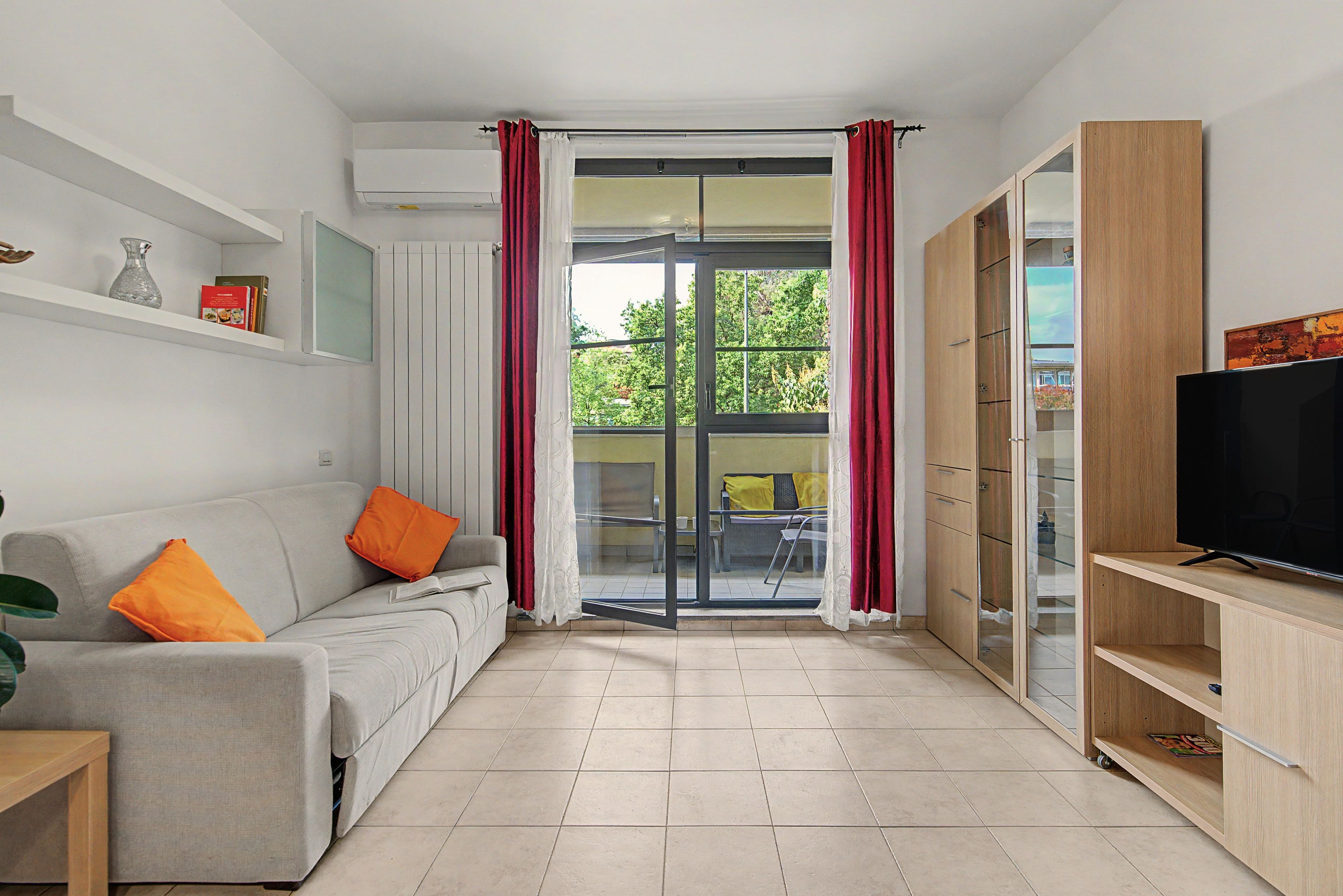 A modern living room with a sofa, a television, and a sliding glass door leading to an outdoor area.