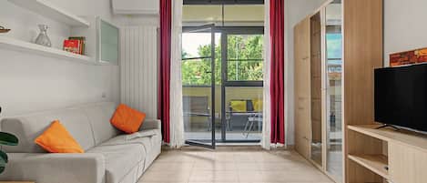 Una sala de estar moderna con un sofá, una televisión y un puerta corrediza de vidrio que da a un área exterior.