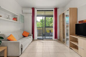 Een moderne woonkamer met een bank, een televisie en een glazen schuifdeur die leidt naar een buitenruimte.