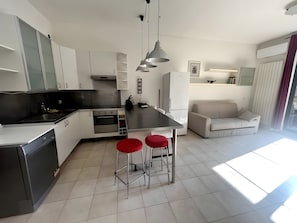 Una cucina moderna con isola centrale, sgabelli da bar, tavolo da pranzo e zona living con divano.