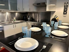 Eine moderne Küche mit Edelstahlgeräten, weißen Schränken und einem Essbereich, gedeckt mit Tellern, Gläsern und Besteck.