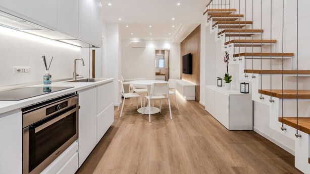 A modern kitchen with white cabinetry, a built-in oven, and a dining area with a round table and chairs. - Cagliari Suite Monti Fly – Renovated Central Apartment Near San Benedetto Market (Cagliari)