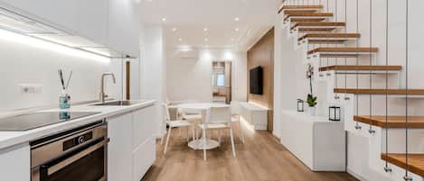 Una cocina moderna con armarios blancos, horno empotrado y un comedor con una mesa redonda y sillas.