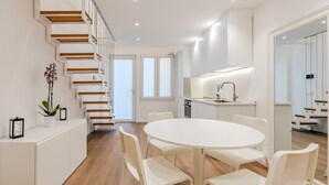 A modern kitchen with white cabinetry, a round dining table, and a staircase with wooden steps. - Cagliari Suite Monti Fly – Renovated Central Apartment Near San Benedetto Market (Cagliari)