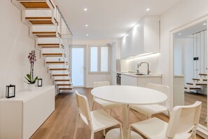 Eine moderne Küche mit weißen Schränken, einem runden Esstisch und einer Holztreppe.