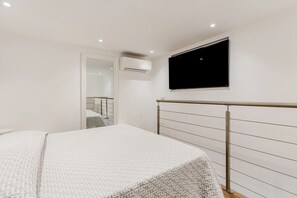 Ein Schlafzimmer mit einem Bett, einem an der Wand montierten Fernseher, einer Klimaanlage und einem Fenster.