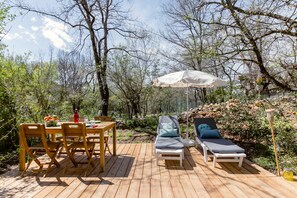 Een houten terras met een tafel, stoelen en een lounge stoel, plus een parasol.