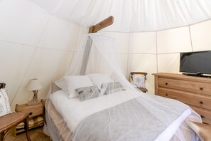 Een bed met hemelbed, een houten nachtkastje met lamp, een dressoir en een televisie.