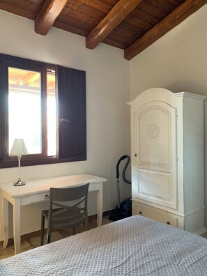 Una stanza con una scrivania, una sedia, un letto, un armadio e una finestra con tende.