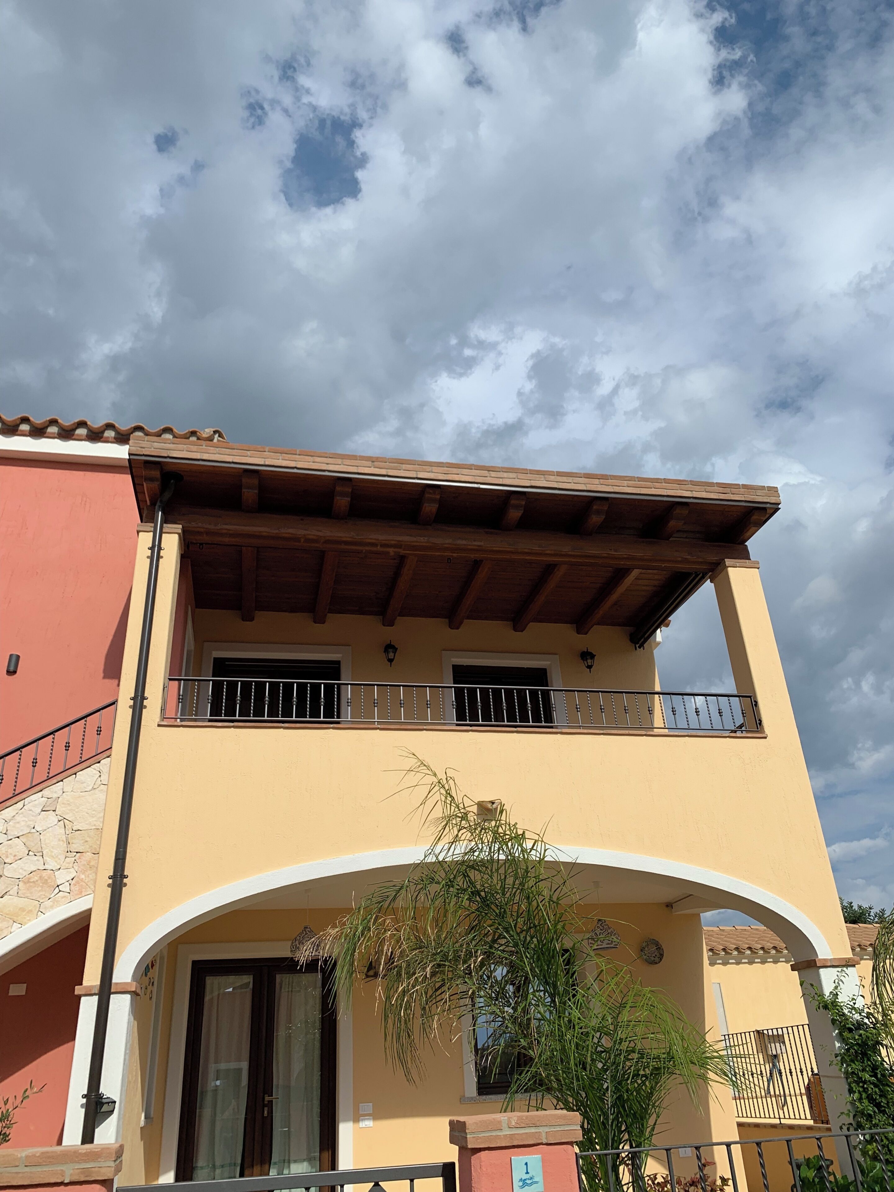 A two-story building with a balcony, a stone wall, and a clear sky.