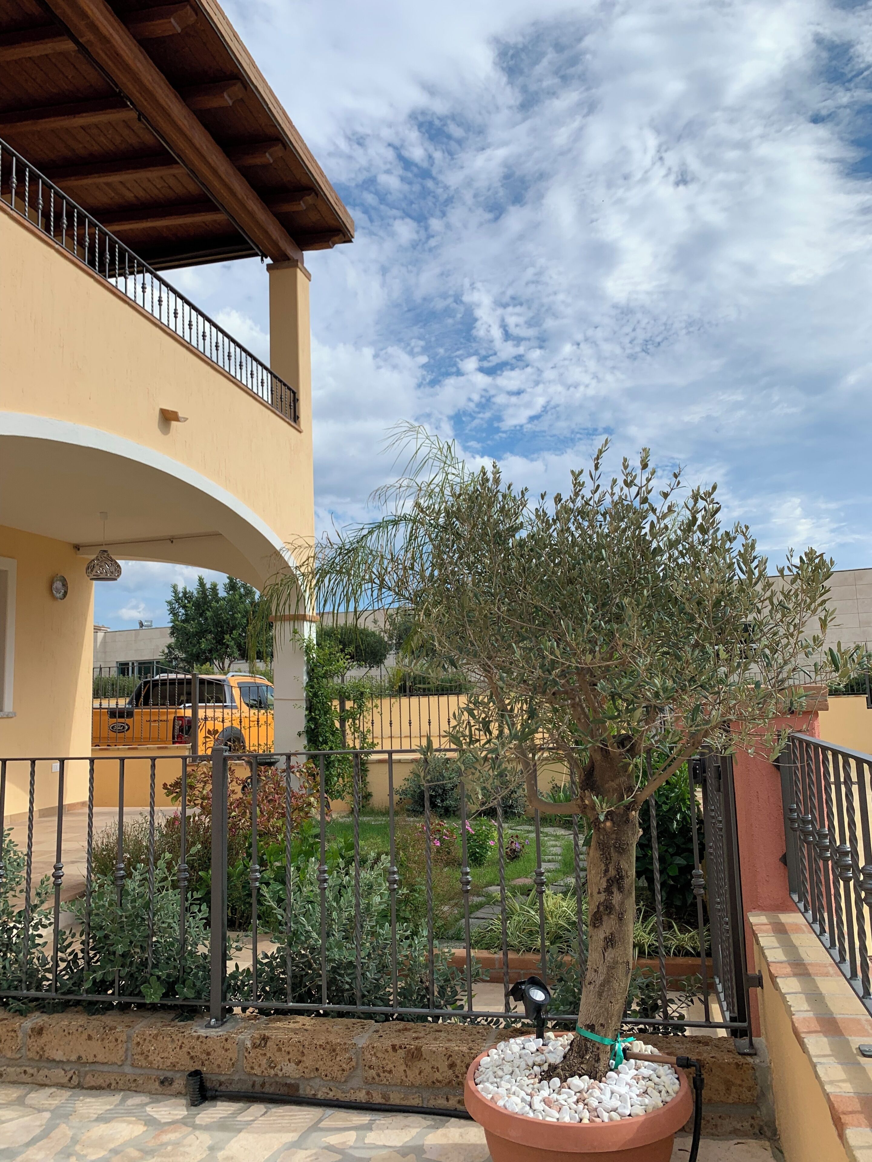 A courtyard with a tree, a potted plant, a yellow vehicle, and a building with a balcony.
