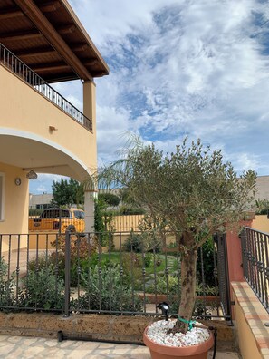 Un cortile con un albero, una pianta in vaso, un veicolo giallo e un edificio con un balcone.