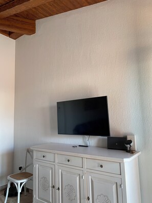 Una stanza con una TV a schermo piatto montata a parete, un mobile bianco con cassetti, uno sgabello e un soffitto in legno.