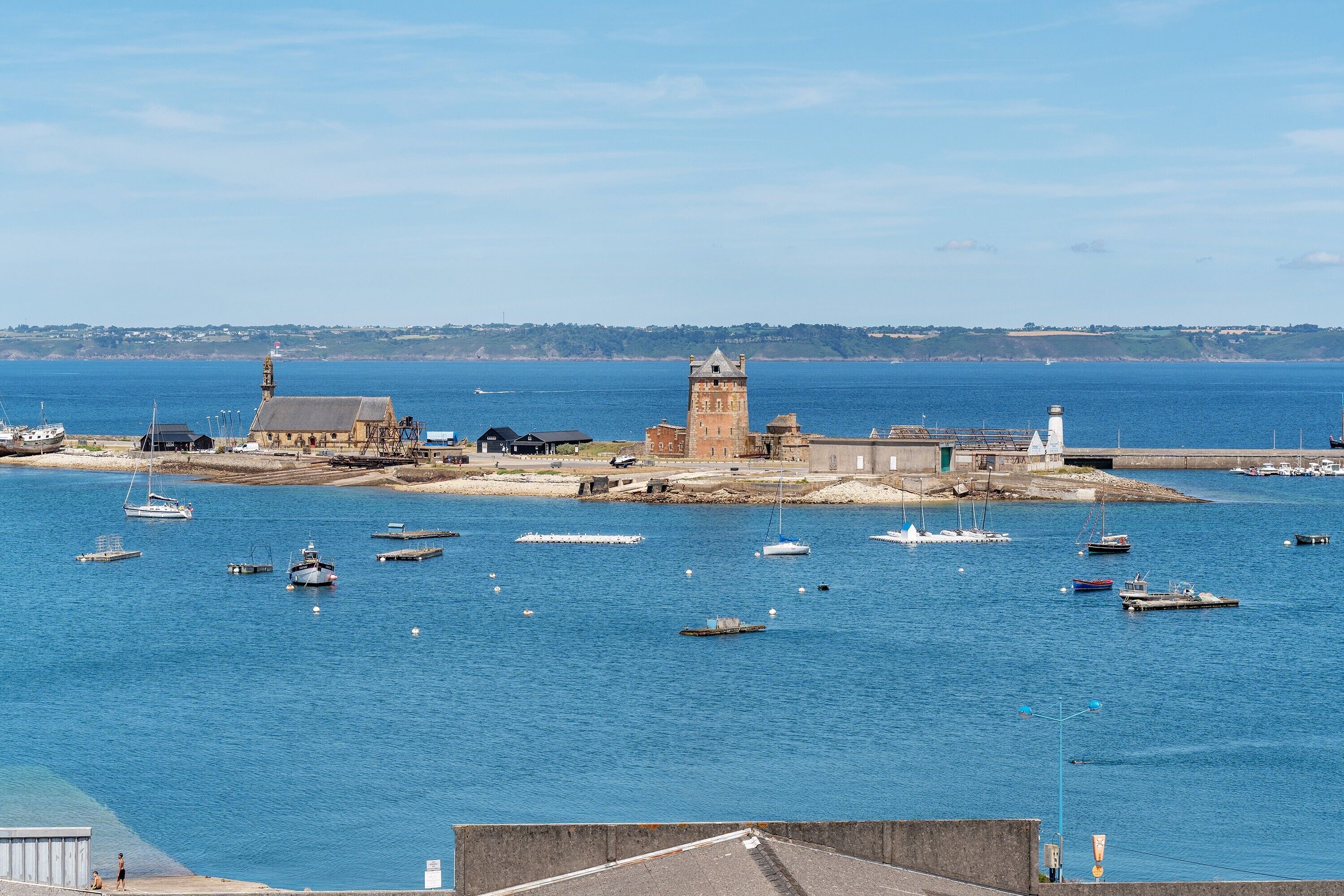 A coastal town with a prominent tower, boats in the water, and a clear view of the sea.
