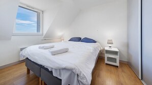 Un dormitorio con cama, mesita de noche, ventana y radiador.