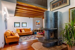 Una sala de estar con chimenea, vigas de madera, un sofá, una alfombra y una planta en maceta.