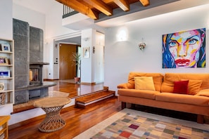 A living room with a fireplace, a sofa, a colorful painting, and a staircase leading to another room.