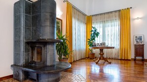 Lareira de pedra, mesa de madeira e cortinas amarelas num quarto com soalho de madeira.