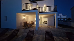 Una casa de dos pisos con un balcón, un comedor con sillas y una mesa, y un patio cubierto.