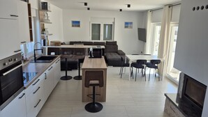 Una cucina moderna con forno a incasso, zona pranzo con tavolo in legno e sgabelli da bar, angolo relax con divano e poltrone, e un camino.