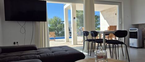 A modern living room with a sofa, a round table with a remote, and a TV mounted on the wall.