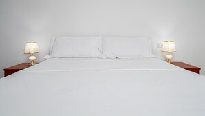 Un letto con lenzuola bianche, due abat-jour con paralumi decorati e una parete bianca liscia.