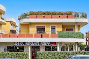 Monikerroksinen rakennus, jonka alakerrassa on pizzeria nimeltä »De’Avu Ristorante Pizzeria».