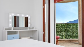 Una camera da letto con una toeletta, un letto, una sedia e vista su un muro verde e montagne.