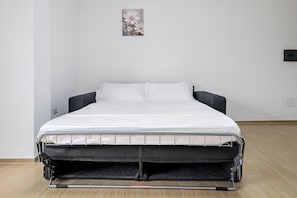 Ein Bett mit einer Matratze und einem schwarzen Gestell, ein an der Wand befestigter Lichtschalter und ein kleines Bild an der Wand.