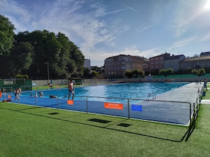 Ein Pool im Freien mit blauer Liegefläche, umgeben von grünem Gras und Bäumen.